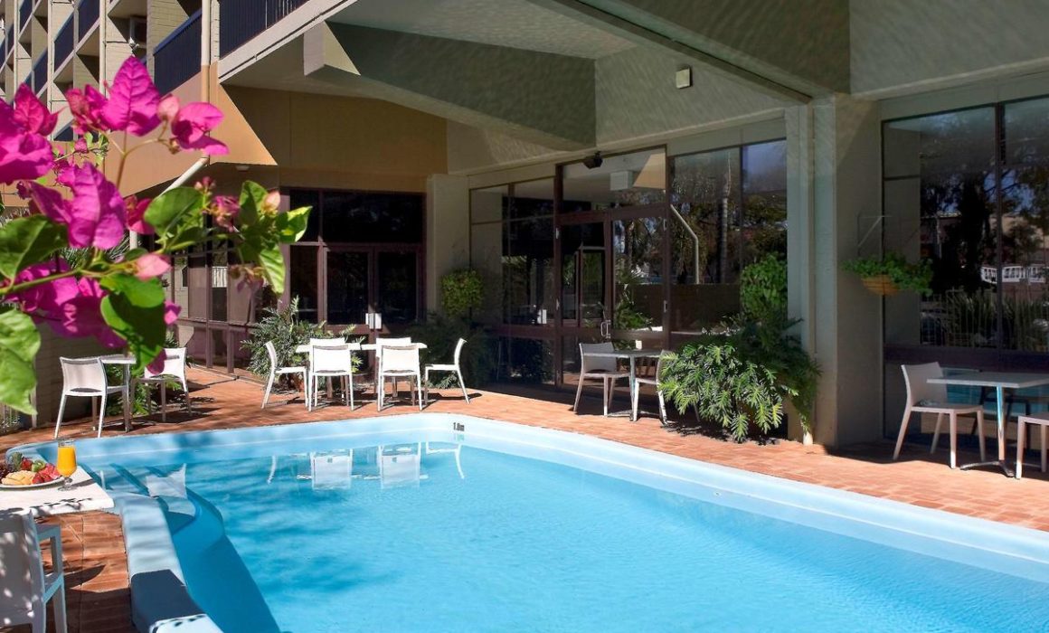 The Kalgoorlie Plaza Hotel outdoor swimming pool is surrounded by greenery and tables and chairs