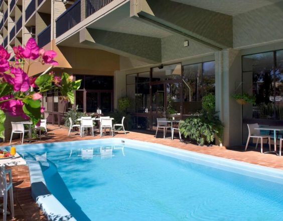 The Kalgoorlie Plaza Hotel outdoor swimming pool is surrounded by greenery and tables and chairs