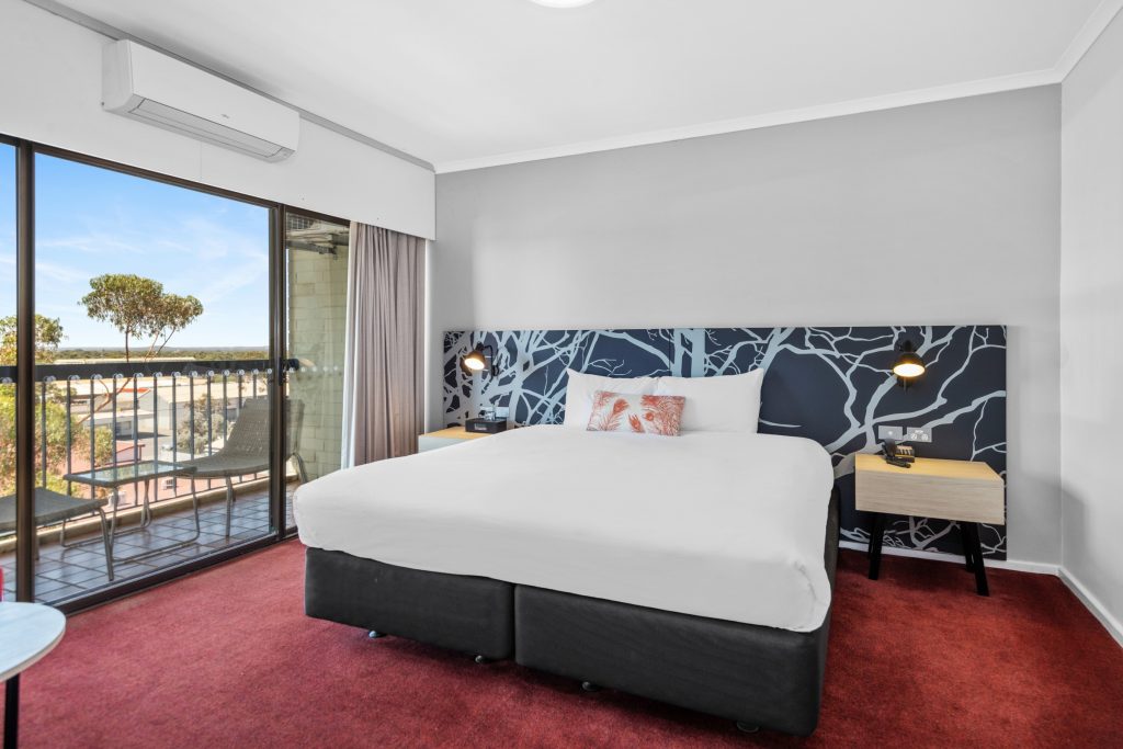 This hotel room at the Plaza Hotel Kalgoorlie features a queen-size bed arranged next to windows that look out onto a private balcony