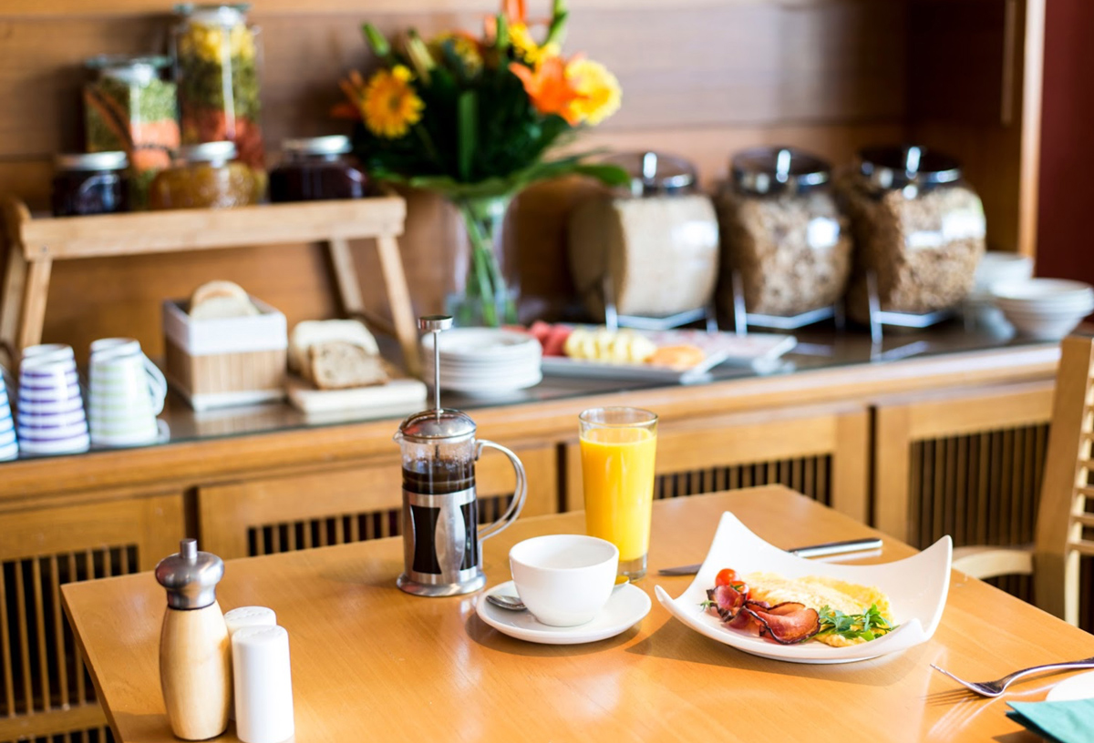 A breakfast bar next to a table with a French press coffee, glass of orange juice, and plate of bacon and eggs