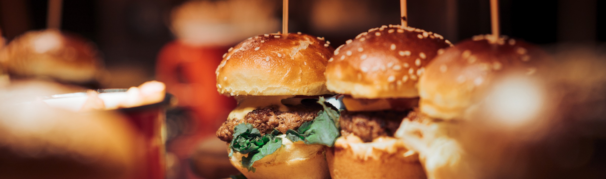 A row of burger sliders with beef patties, lettuce, and cheese