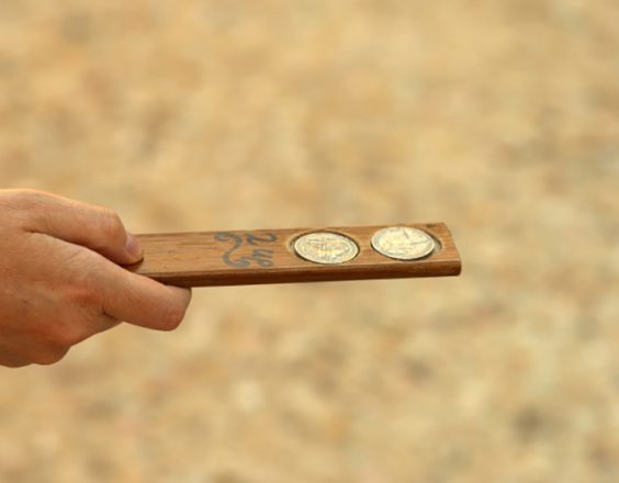 A Two Up player holds a small, thin, plank of wood holding two coins, ready to throw