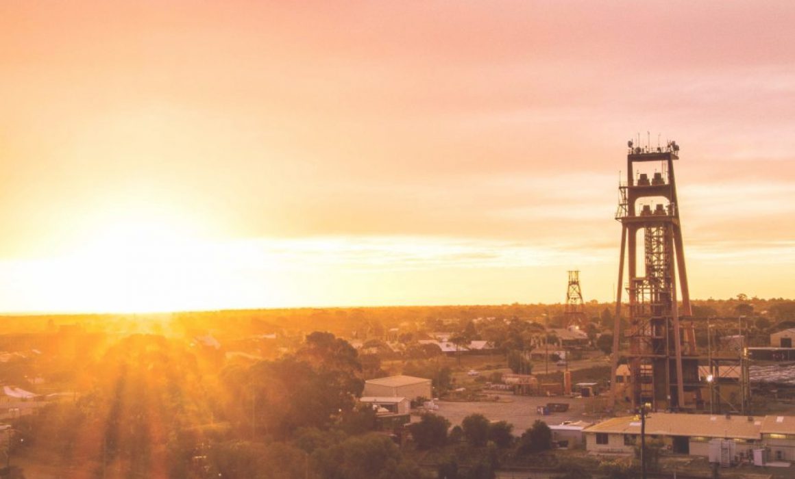 A panoramic view of Kalgoorlie, with the sunset shining over the town's buildings, trees, and mining architecture