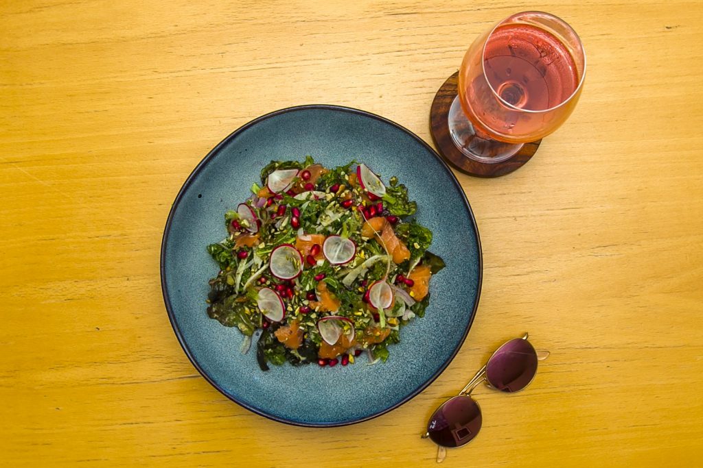 A salad with pomegranate, radish, and orange segments served with a glass of rose