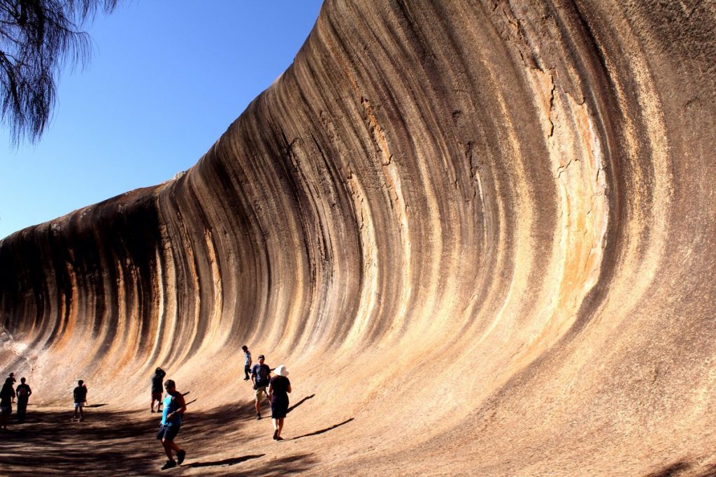 A large wave-like rock formation with tourists walking along the bottom edge.